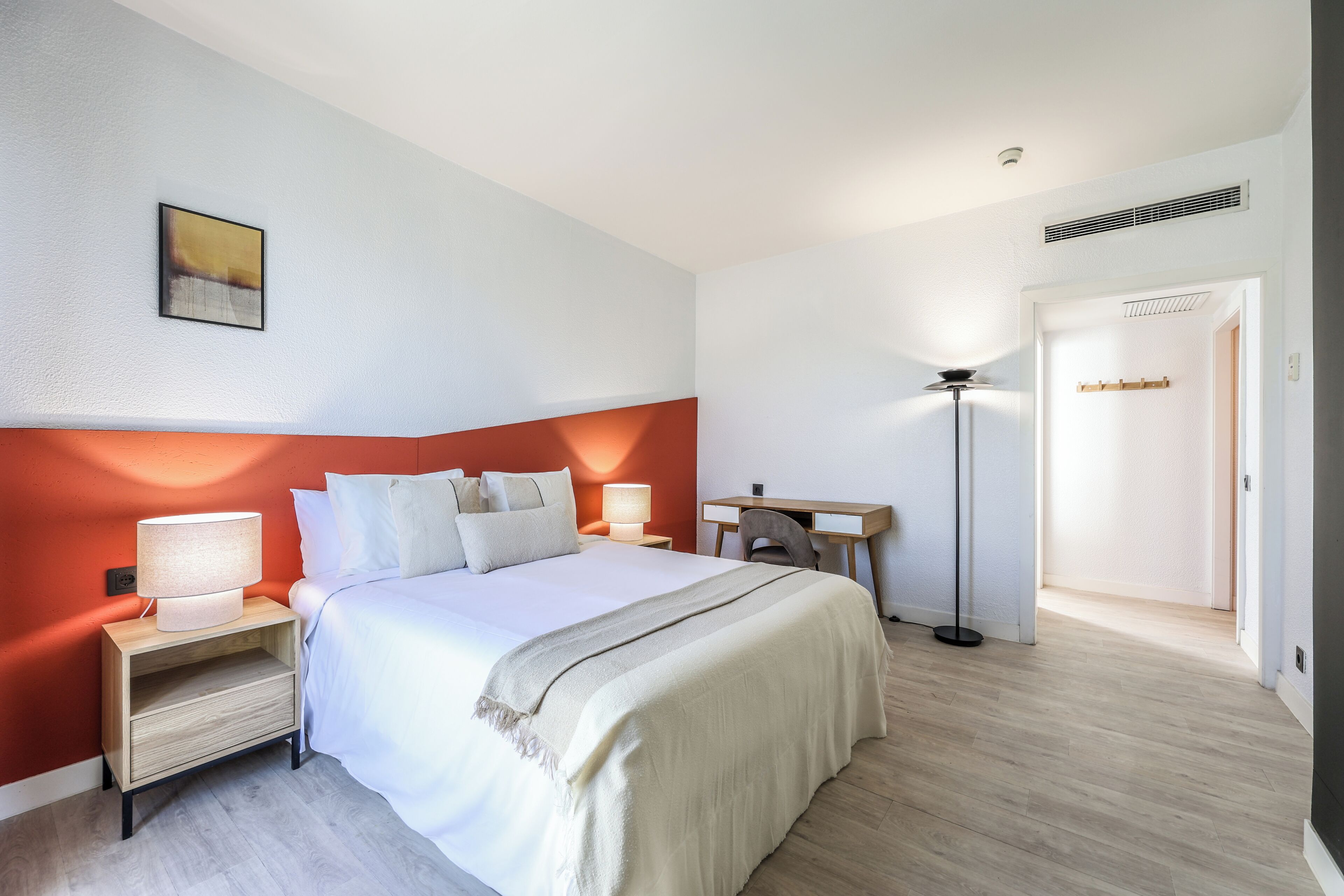 A hotel room with a bed, bedside tables, a desk, and a lamp.