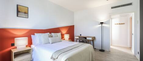 A hotel room with a bed, bedside tables, a desk, and a lamp.