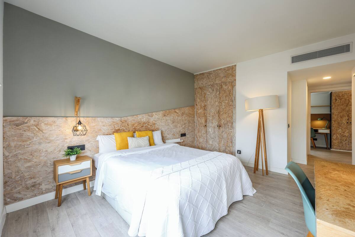 Un dormitorio moderno con cama, mesita de noche, lámpara y vista a otra habitación.