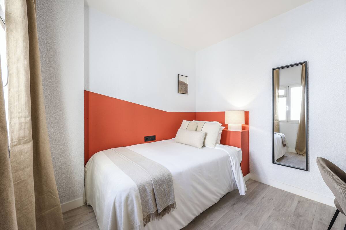 Una habitación de hotel con cama, mesita de noche, espejo y silla.