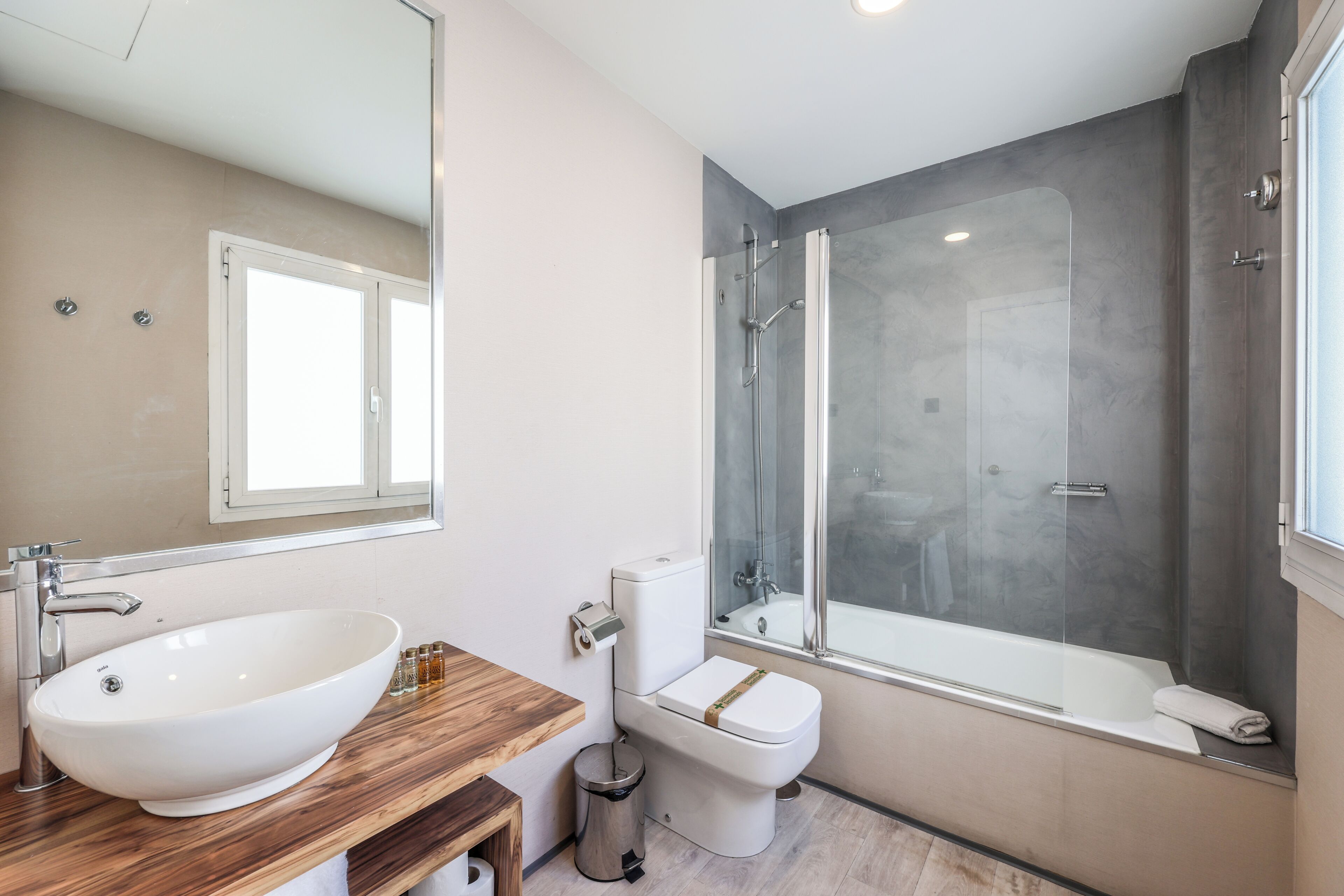 A modern bathroom with a large white sink, a toilet, and a glass-enclosed shower.