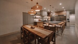 Eine moderne Küche mit Holzschränken, einer zentralen Kochinsel mit Barhocker, Pendelleuchten und integrierten Geräten.