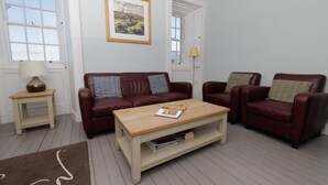 A living room with a brown leather sofa, two armchairs, a wooden coffee table, and a framed landscape painting on the wall.