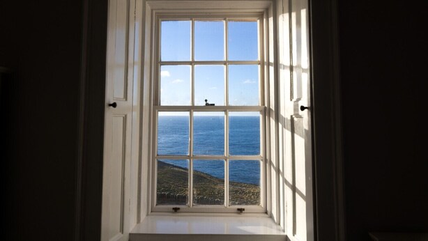 A view through a window with a clear sky and the sea visible beyond.