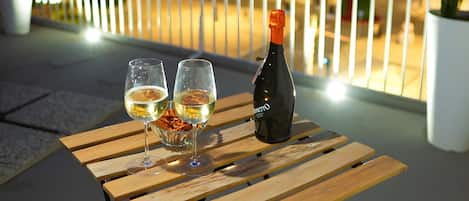 A wooden table with two glasses and a bottle on a balcony at night.