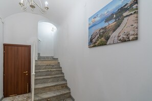 Un escalier en marbre menant à une pièce, une porte en bois et un tableau représentant un paysage côtier, accroché au mur.