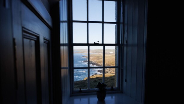 A window with a view of the ocean and rocky coastline.