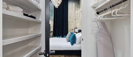 A bedroom with a bed, a chandelier, a wardrobe, and a hanging rack.