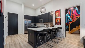 Una cocina moderna con una isla central, armarios negros, electrodomésticos de acero inoxidable y una zona de bar con taburetes.