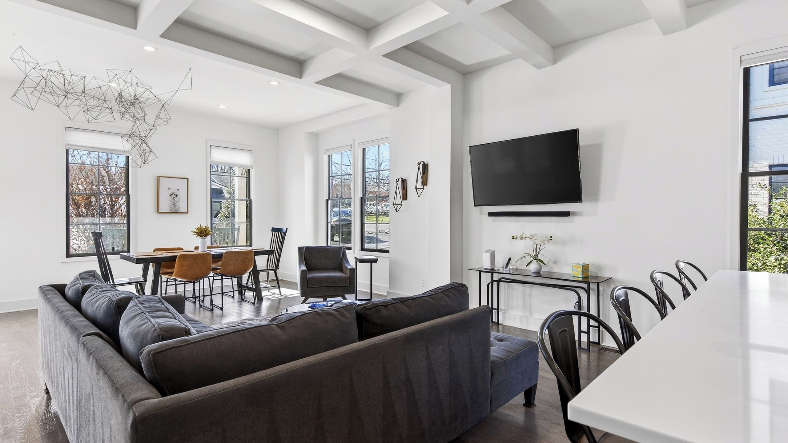 A modern living room with a sectional sofa, dining area, and a TV mounted on the wall.