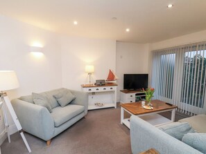 A modern living room with a grey sofa, a wooden coffee table, a white TV stand, and a lamp. - ONE Union Mill - Garden Apartment (Whitby)