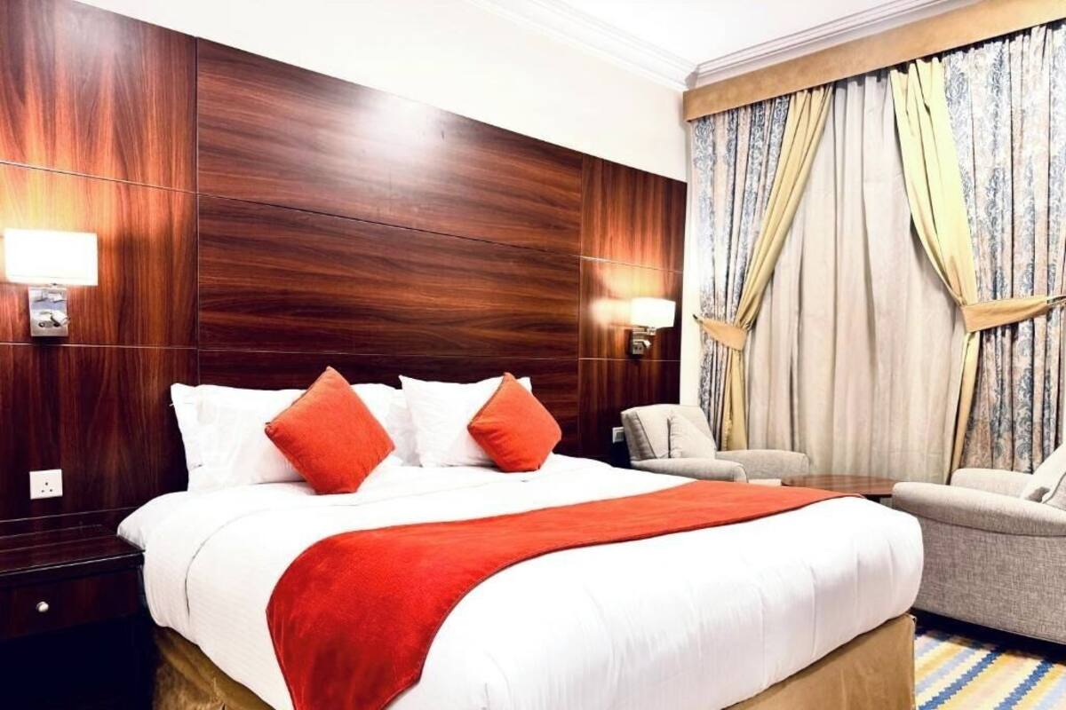 Ein Hotelzimmer mit einem großen Bett, einem Holzkopfstück, zwei Nachttischlampen, einem Sofa und einem gemusterten Teppich.