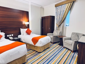 A hotel room with two beds, a sofa, a chair, a desk, and a large window with curtains. - Rowaa Lindy Hotel Makkah (Makkah)