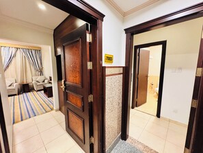 A hotel room with a wooden door, a sign with the number 7003, a bathroom with a toilet and sink, and a living area with a sofa and curtains. - Rowaa Lindy Hotel Makkah (Makkah)