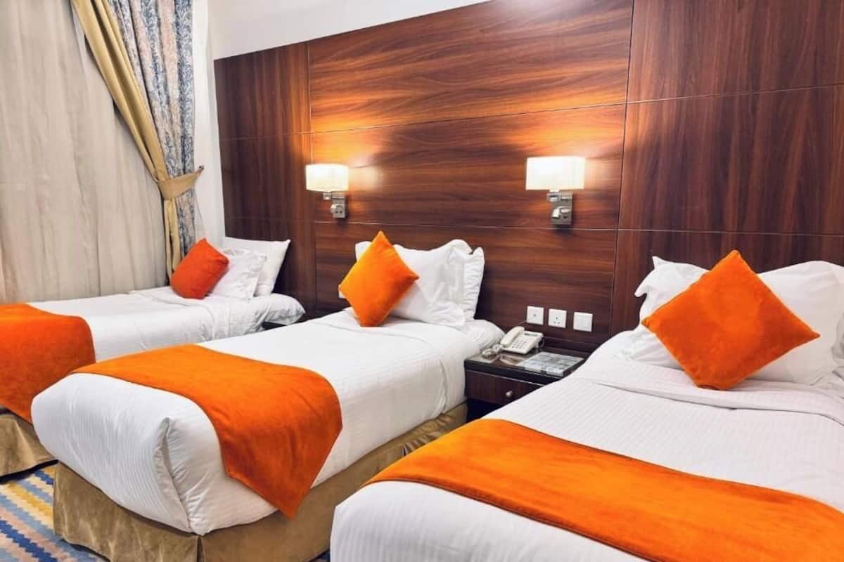 Ein Hotelzimmer mit zwei Betten, jeweils mit weißer Bettwäsche und orangefarbenen Akzenten, einem Holzkopfschild und Nachttischlampen.