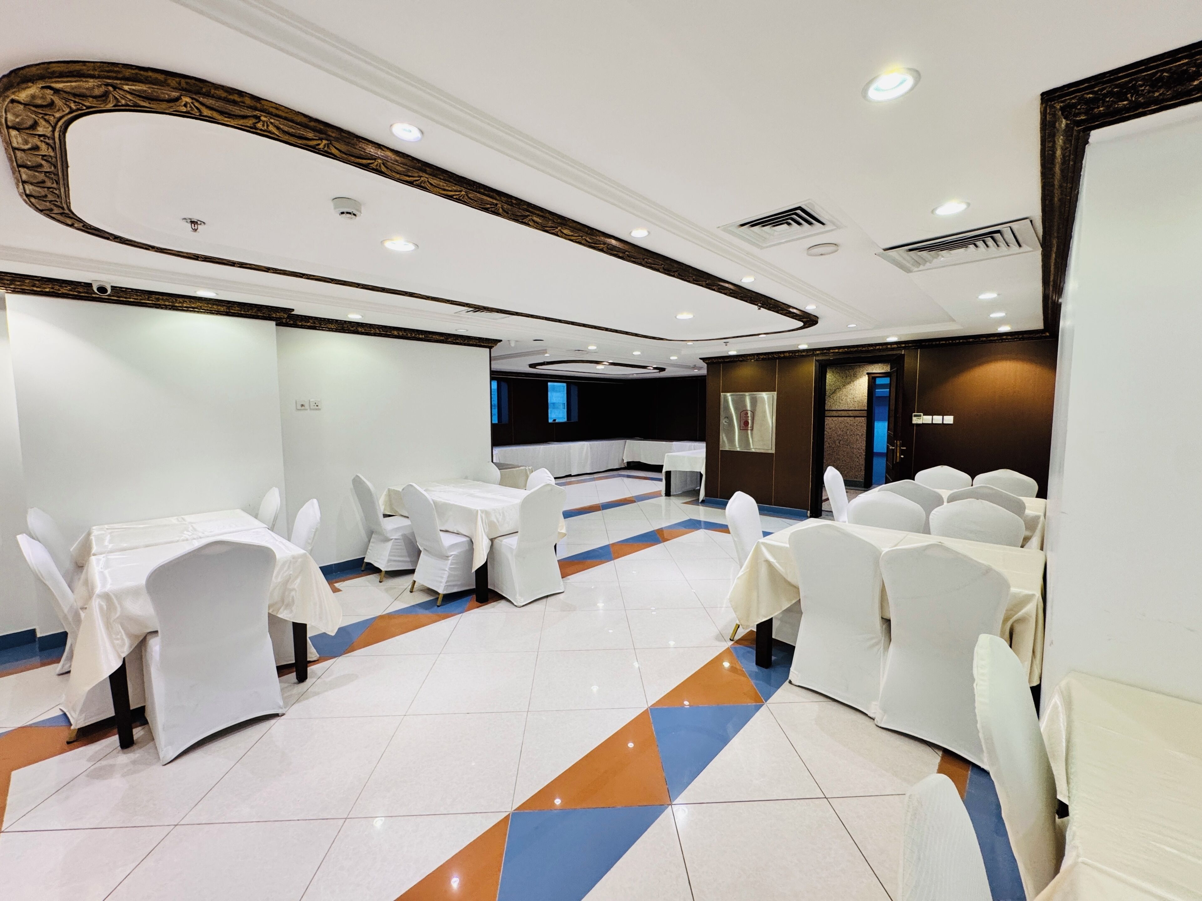 A banquet hall with round tables, white chairs, and a patterned floor.
