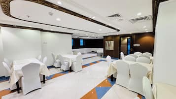 A banquet hall with round tables, white chairs, and a patterned floor.