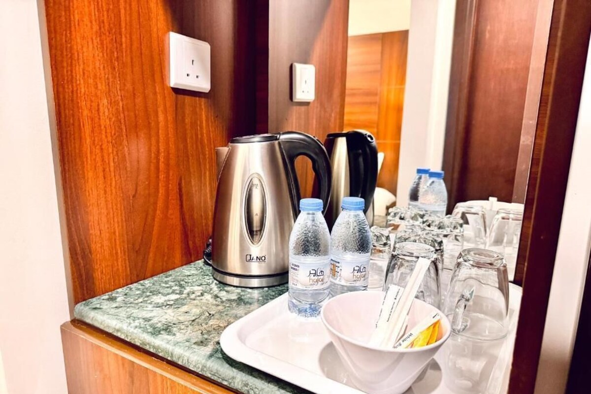 Una encimera de cocina con un hervidor, botellas de agua, vasos y una bandeja con un cuenco y utensilios.