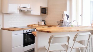Una cocina moderna con armarios blancos, horno empotrado, microondas y encimera de madera. Hay dos taburetes blancos en la isla.