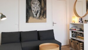 Una sala de estar moderna con un sofá negro, una mesita de madera, un cuadro de un tigre, una estantería y un espejo redondo.