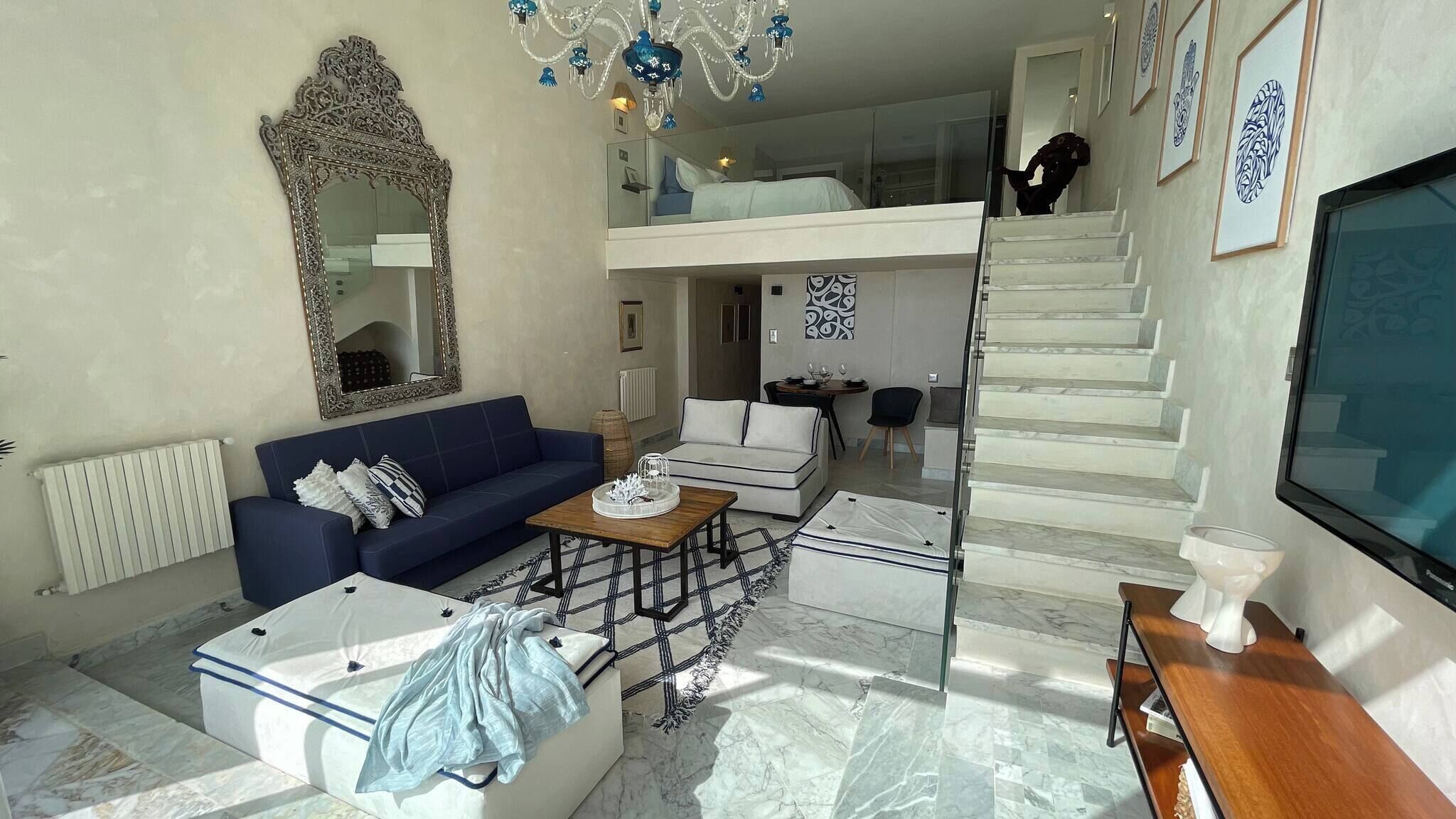 Un vaste espace de vie comprenant un canapé bleu, un canapé blanc, une table basse et un escalier menant à un niveau supérieur.