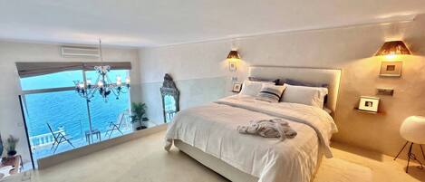 A bedroom with a large bed, a view of the sea, and a balcony with outdoor furniture.