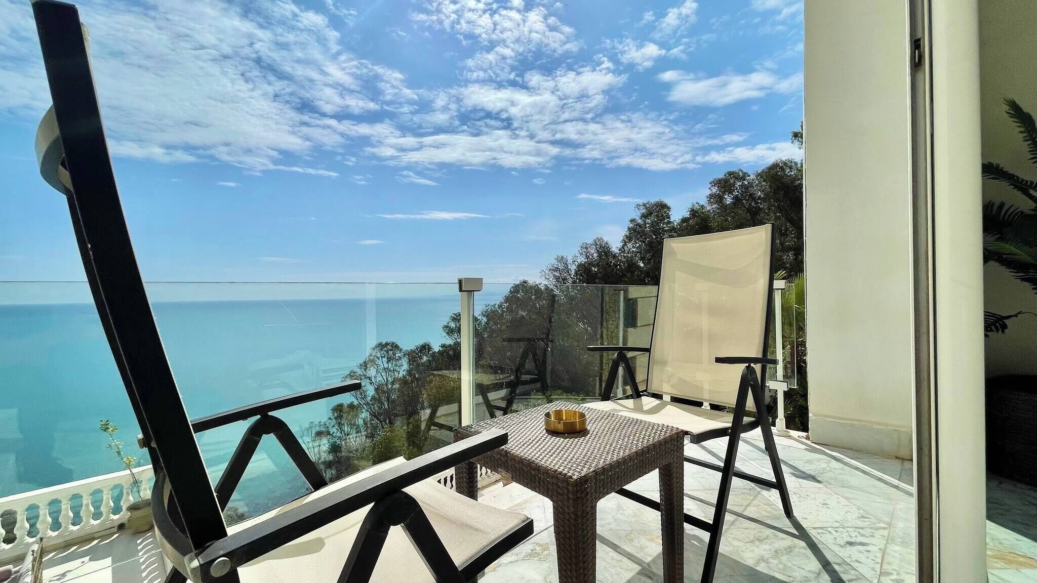 Un balcón con vista despejada al mar, una mesa de mimbre y una silla.