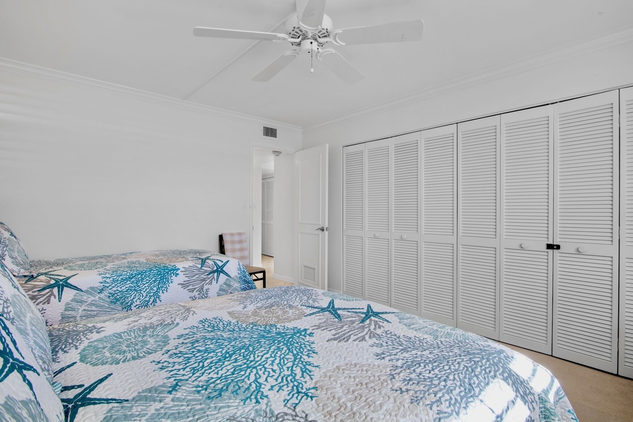 A bedroom with a bed, a ceiling fan, a closet with louvered doors, and a door leading to another room.