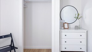 Une commode blanche, ornée d’un miroir rond, d’un tableau encadré et d’un vase contenant une plante.