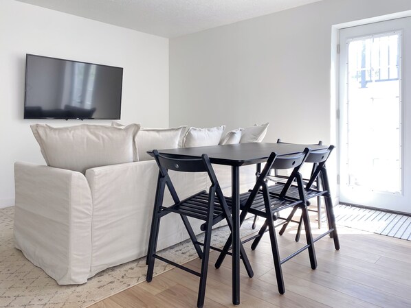 Un salon moderne avec un canapé, une table à manger et des chaises. Un téléviseur à écran plat est fixé au mur.
