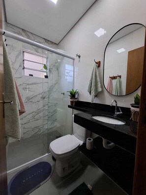 Ein modernes Badezimmer mit einer Duschkabine aus Glas, einer weißen Toilette, einem schwarzen Waschbecken und einem runden Spiegel.