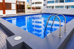 A rectangular swimming pool with metal ladders, a lifebuoy, and a tiled deck area. - Neptuno Apartment in the Center of Candelaria (Candelaria)