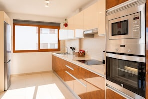 A modern kitchen with a stainless steel refrigerator, oven, and microwave. There is a window with blinds, a sink with a faucet, and wooden cabinets. - Neptuno Apartment in the Center of Candelaria (Candelaria)