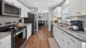 A modern kitchen with stainless steel appliances, white cabinetry, and a wooden floor. - Right on parkway! Playground~Hot Tub~Fire Pit (Pigeon Forge)
