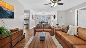 A modern living room with a brown leather sofa, a wooden coffee table, and a ceiling fan. - Right on parkway! Playground~Hot Tub~Fire Pit (Pigeon Forge)