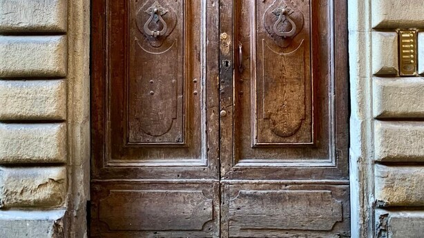 A wooden double door with a glass transom above, set within a stone archway. - Between Duomo and Tower of Arnolfo, double view (Firenze)