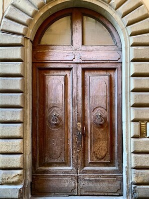A wooden double door with a glass transom above, set within a stone archway. - Between the Cathedral and the Arnolfo Tower, a Double View (Firenze)