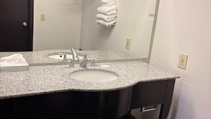 Une salle de bain avec un lavabo doté d’un plan de toilette en granit, un meuble-lavabo foncé, un porte-serviettes avec des serviettes pliées et un miroir.