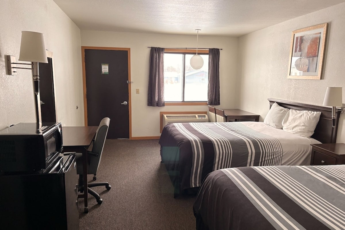 A hotel room with two beds, a desk, a chair, a TV, and a window with curtains.