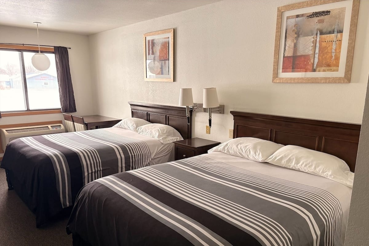 A hotel room with two beds, each with striped bedding, a nightstand with a lamp, and a framed picture on the wall.