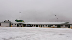 Un motel avec une rangée de chambres, une pompe à essence et un garde-manger, ainsi qu’un grand parking recouvert de neige.