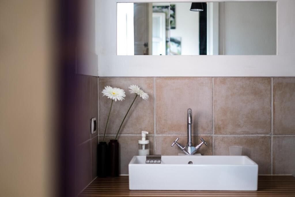 Un baño moderno con un lavabo rectangular, un espejo encima y dos jarrones con flores blancas.