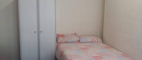 A bedroom with a bed, a wardrobe, and a small table.