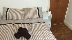 A neatly made bed with striped bedding and two pillows, a white bedside table with a single drawer, and a wooden floor. - MIdway Hotel  (Blackpool)