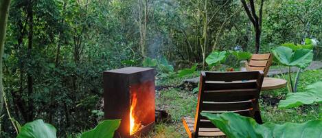 A fire pit with a table and chairs in a forested area.