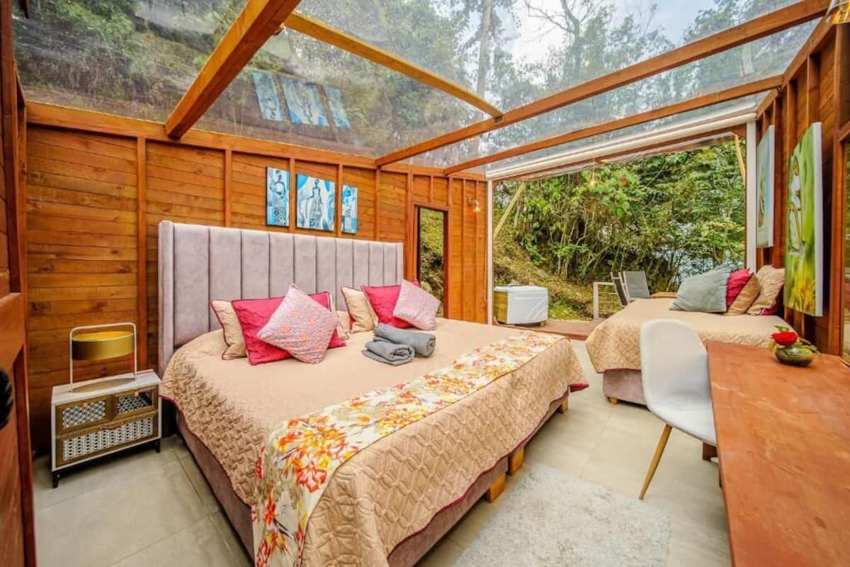 Ein gemütliches Schlafzimmer mit einem großen Bett, einem Schreibtisch und Blick auf den Wald.