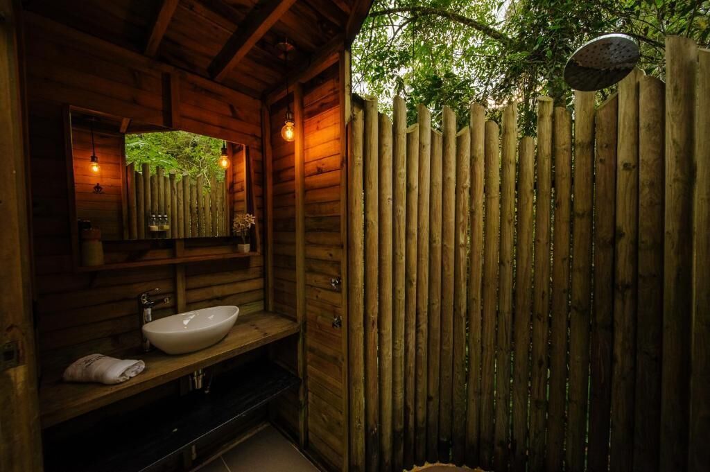 Ein Badezimmer einer Holzhütte mit einem Holzwaschbecken, einem Spiegel und einer hängenden Duschbrause.