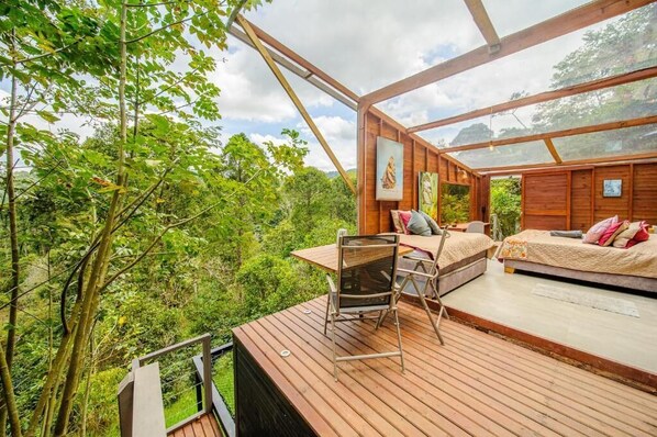A wooden deck with a table and chairs, a bed, and a painting on the wall. - Terramaga Glamping (San Francisco)