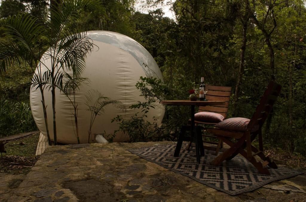 Une structure sphérique située dans un jardin luxuriant, avec une table et une chaise en bois.