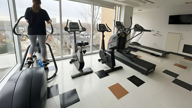 A gym with various exercise equipment, large windows, and a flat-screen TV on the wall. - Saint-paul Residence (Ottawa)